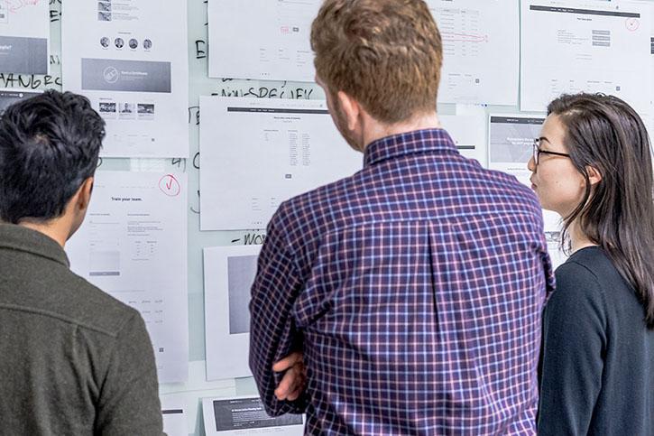 Three people looking at a project workflow board