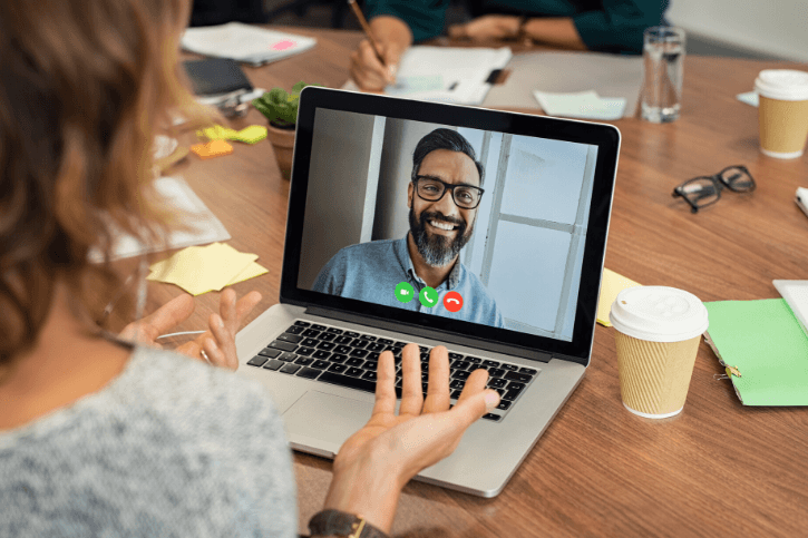 A bearded man on a laptop screen meets with someone we see only the back of.