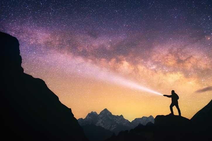 Person in darkness lighting the way with a flashlight.