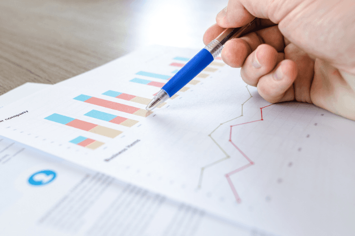 A hand hold a pen pointing to bar charts on a printed report