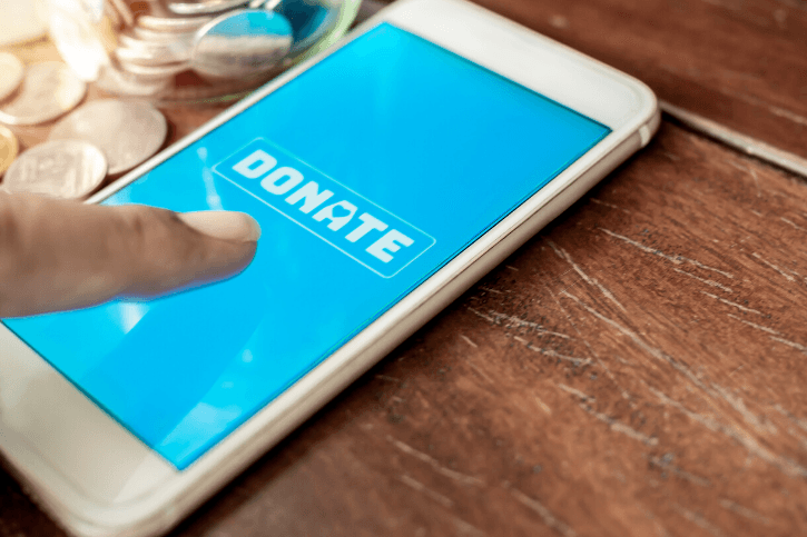 "DONATE" appears in white on a blue phone screen. An index finger hovers above the phone.