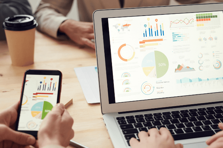 Unseen people use a phone and laptop displaying colorful analytics.