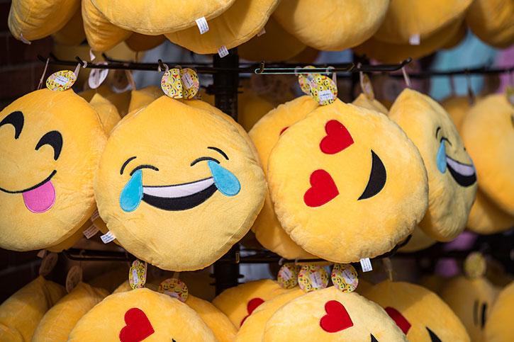 Emoji plush toys hang on a rack: Crying, heart eyes, hungry