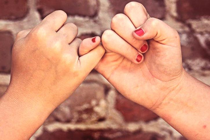 Two people share a "pinky swear" where their two pinky fingers are entwined, as a gesture of friendship.