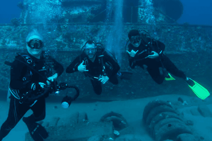Three people in the ocean wearing scuba gear, smiling at the camera.